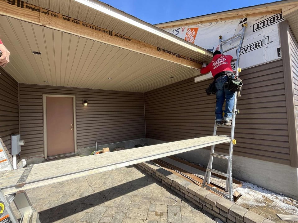 Contractor installing siding and soffit under roof overhang on back patio in Burton MI
