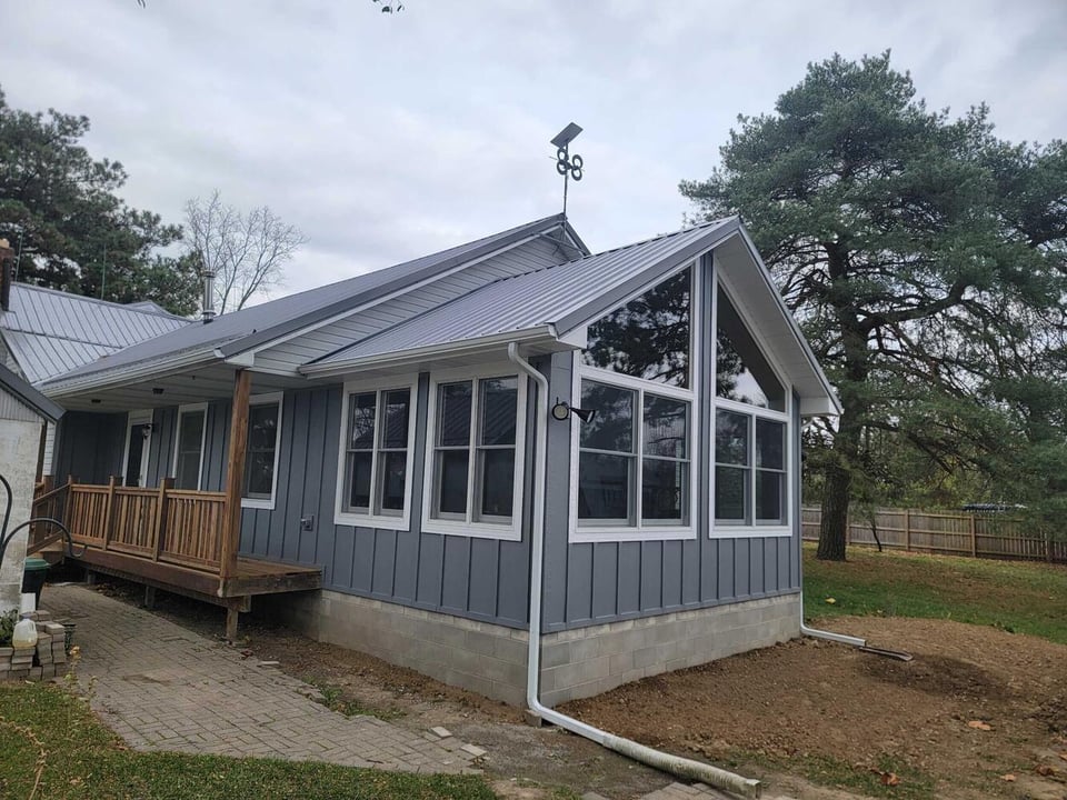 Gray home addition with large windows, metal roof, and porch in Genesee County, MI by Swank Builders