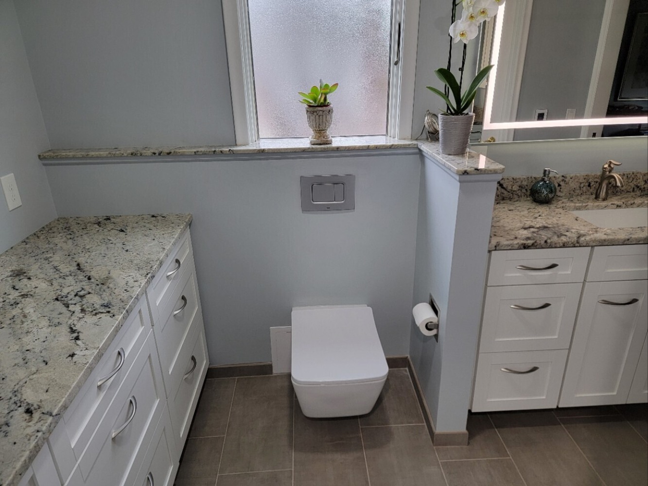 Swank Builders Inc bathroom remodel featuring wall mounted toilet with custom cabinetry and granite countertops in Burton MI