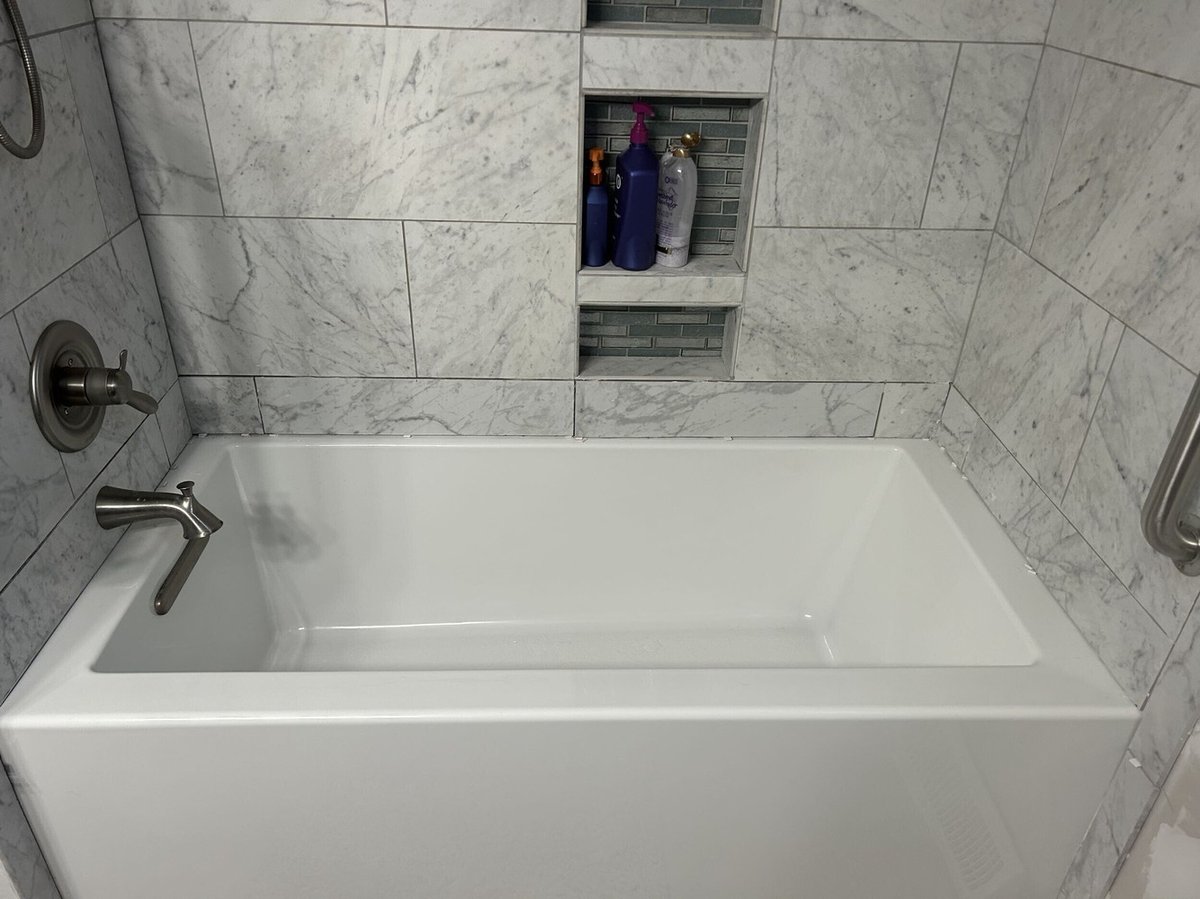 bathtub with marble look tile surround and recessed niche by Swank Builders Inc in Burton MI