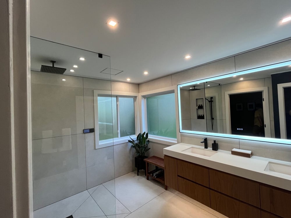 modern double vanity bathroom with backlit mirror and custom cabinetry by Swank Builders Inc in Burton MI