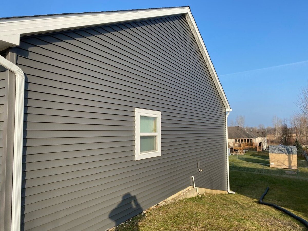Side view of home with grey horizontal siding, white trim, and downspout on sloped yard by Swank Builders Inc in Genesee County MI