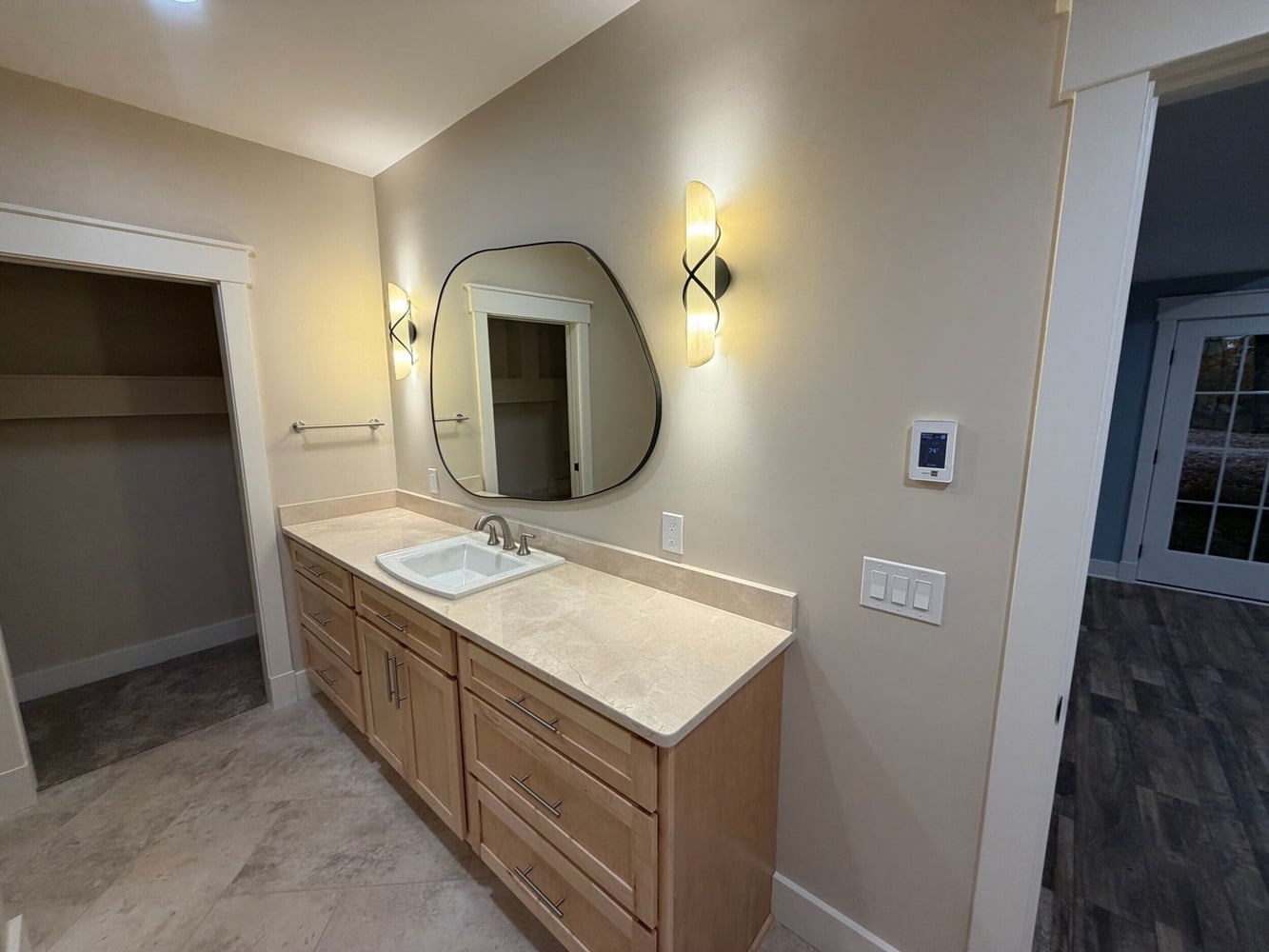custom home bathroom featuring round mirror, vanity lighting, and stone countertop in Michigan
