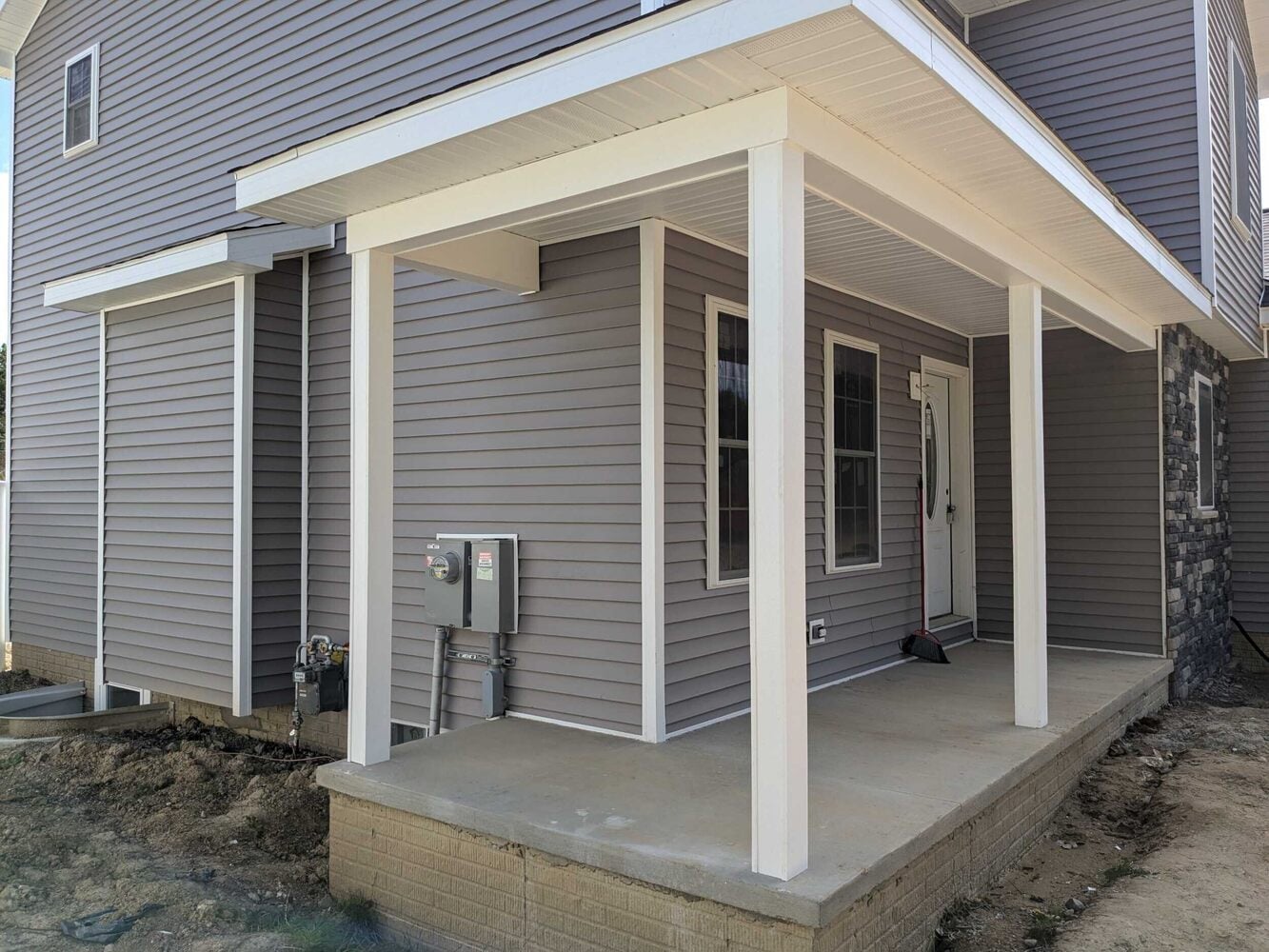 Covered back porch with white posts, grey vinyl siding, and concrete slab on new home in Fenton MI