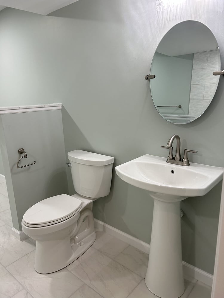 Basement bathroom with pedestal sink, round mirror, and light green walls in Goodrich MI