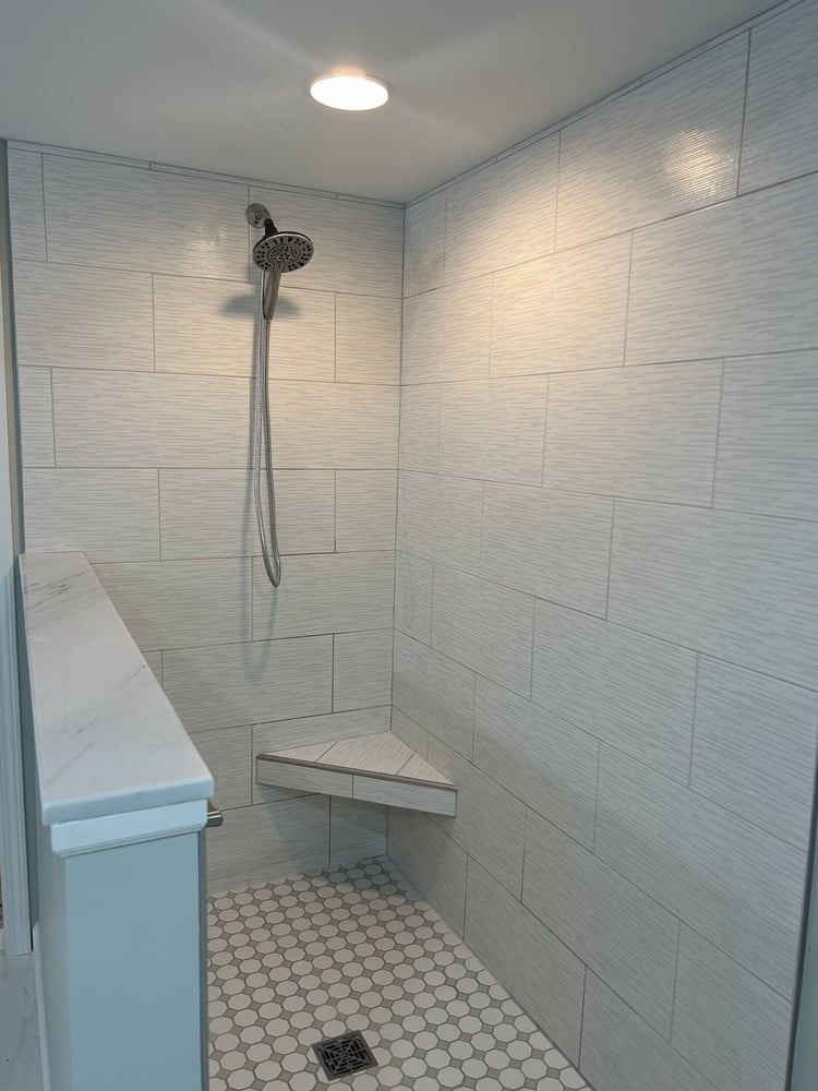 Custom tile shower with built in corner bench, hex tile floor, and handheld shower head in Goodrich MI